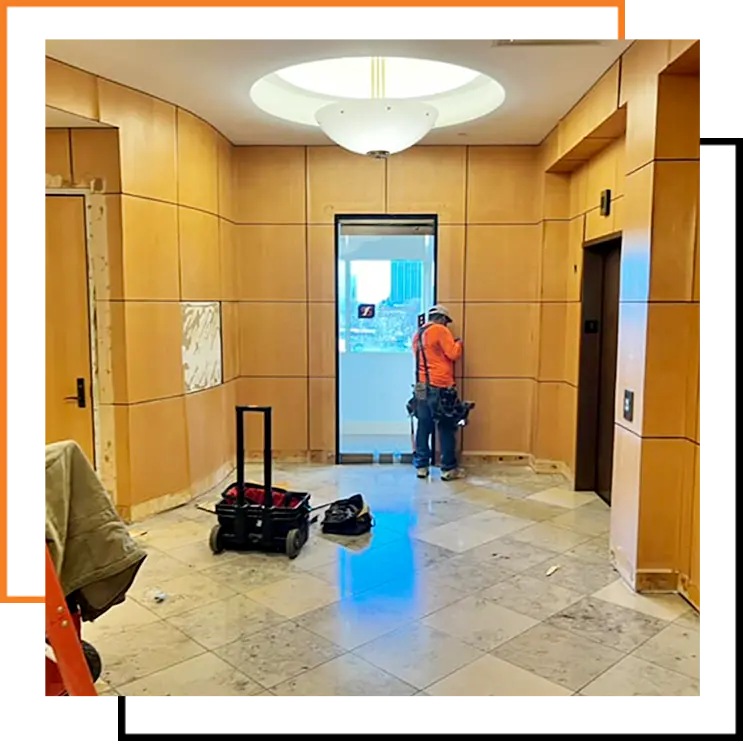 Construction worker performing interior renovation work in a commercial building lobby near an elevator